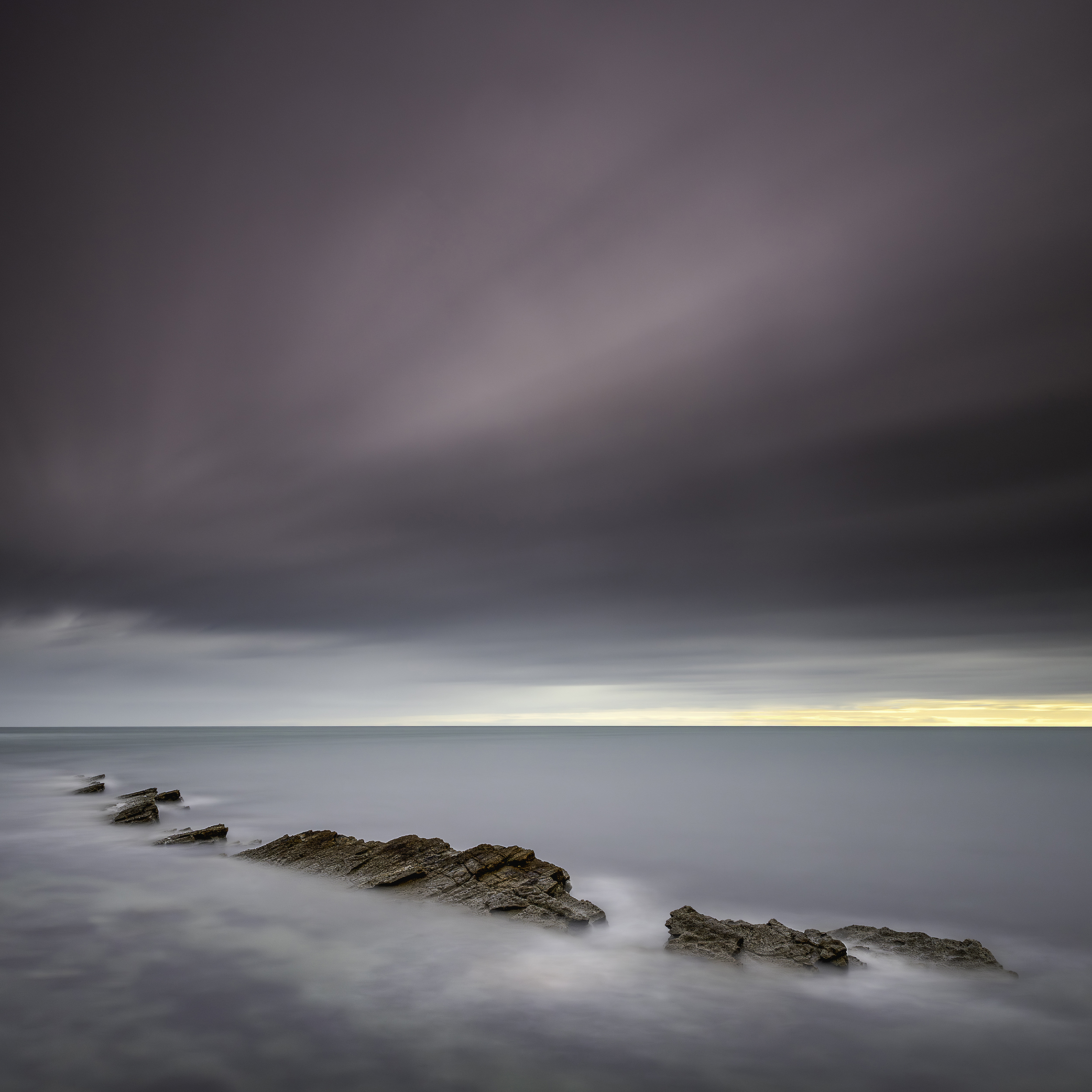 Cutting Through Calm — rocks emerging through muted long-exposure water beneath a quiet sky