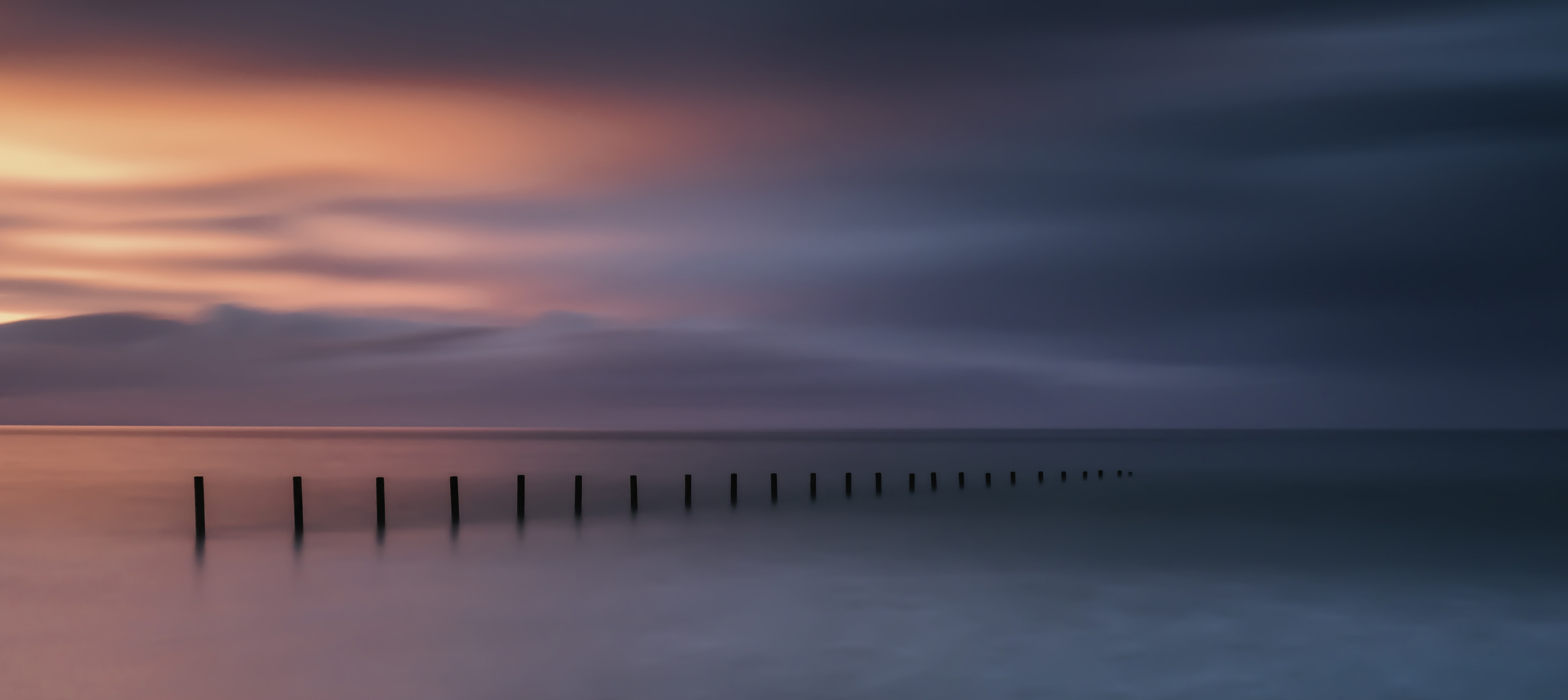 Sunset Strand — a receding line of posts extending through pastel long-exposure water